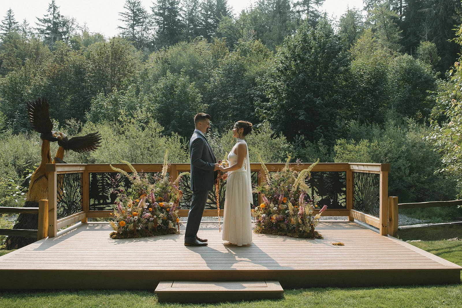 Newlyweds holding hands on the wooden alter deck at Tahuya River Lodge, overlooking the River and forested landscape
